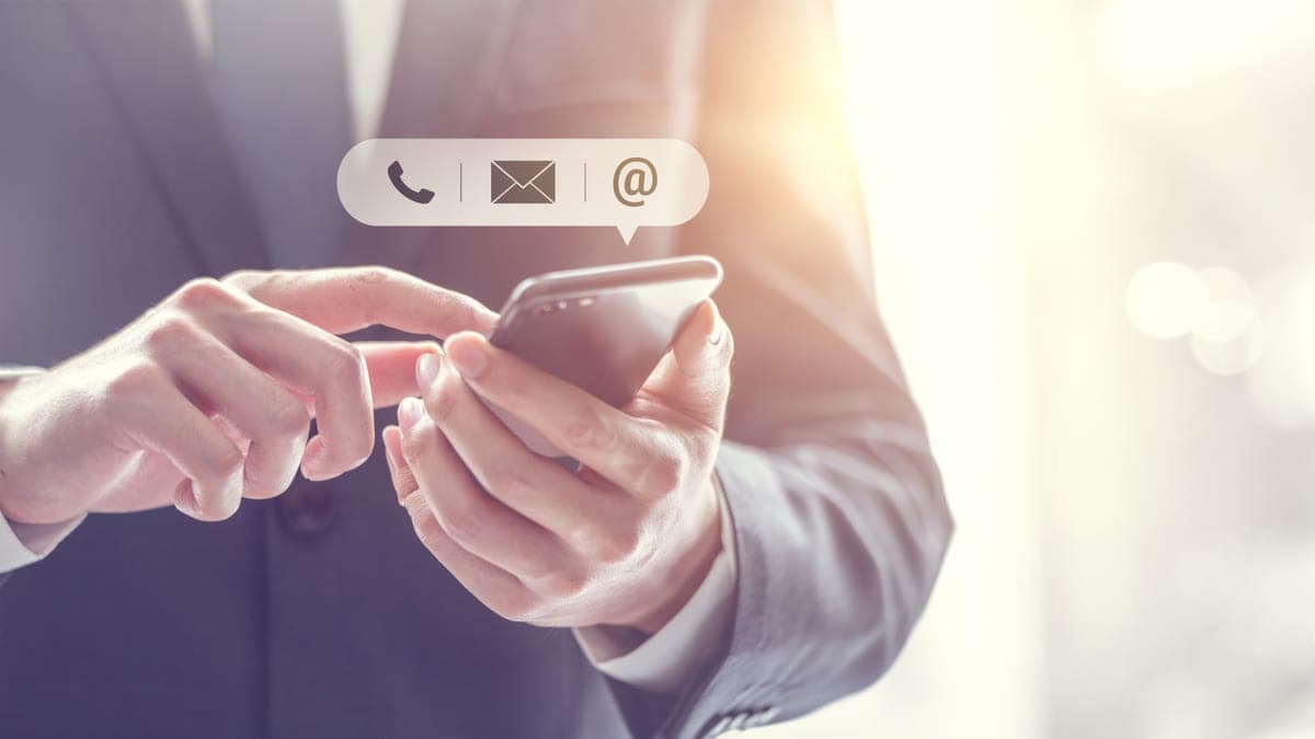 Geschäftsmann bedient ein Smartphone mit schwebenden Symbolen für E-Mail und Kontakt, Sinnbild für Newsletter-Versand