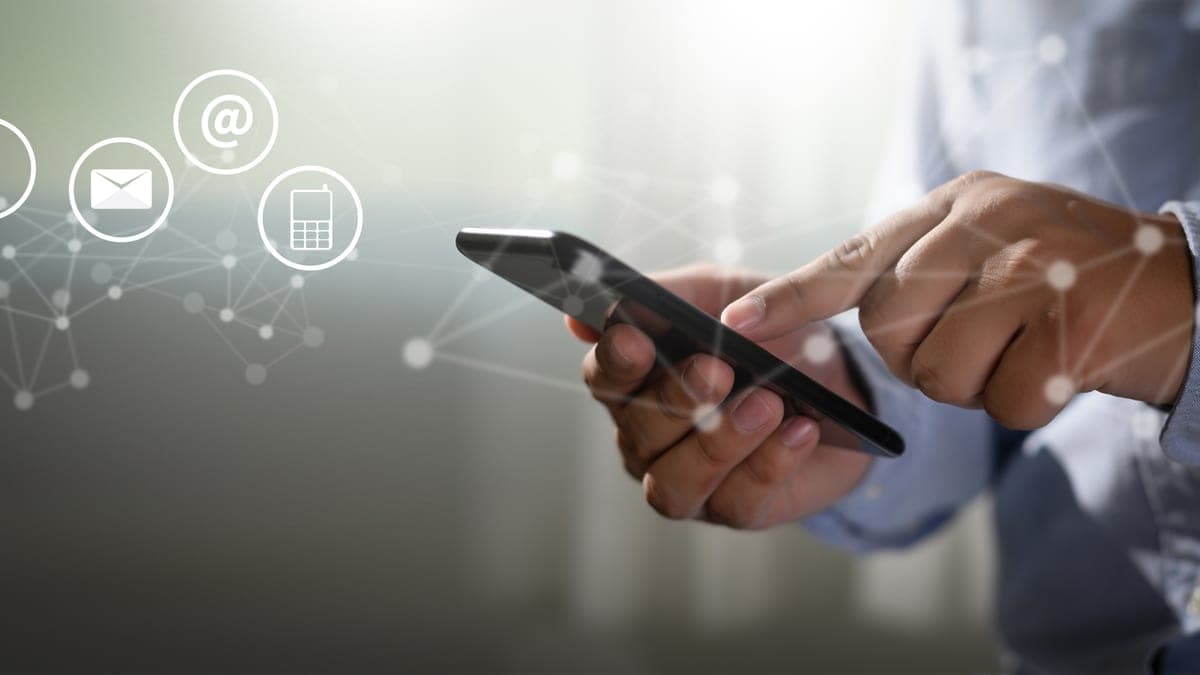 Hände bedienen ein Smartphone, daneben schwebende Kontakt-Symbole für Telefon und E-Mail, Sinnbild für Team-Kommunikation per App